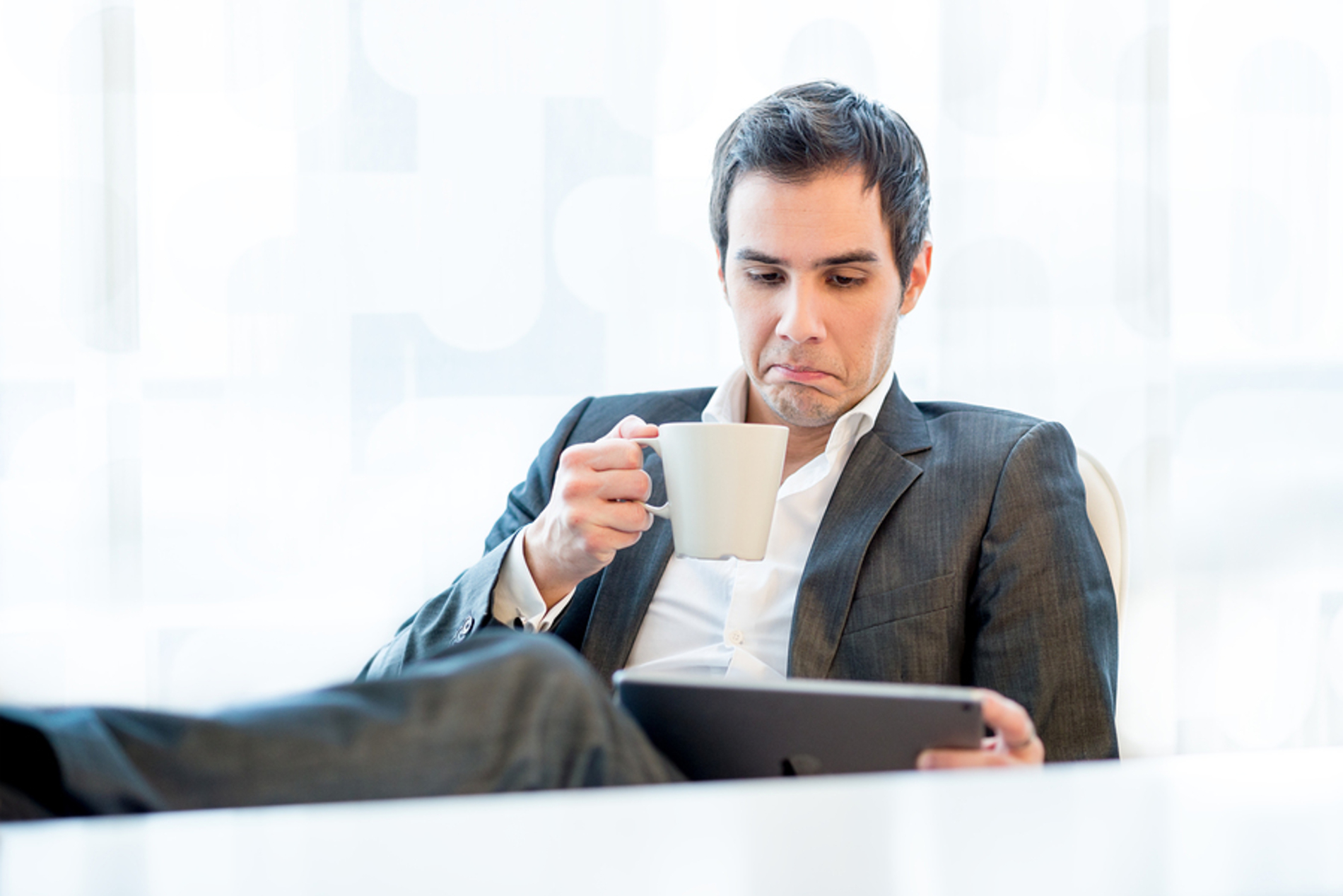 Man looking at his tablet while drinking a coffee.